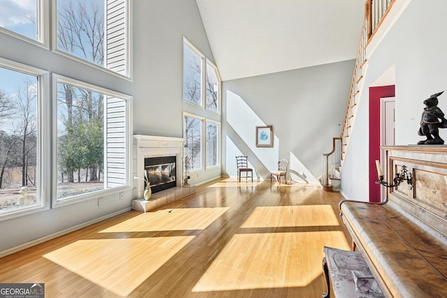 living area featuring high vaulted ceiling, wood finished floors, a tiled fireplace, and stairs