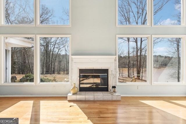 living area featuring light wood-style flooring, a tile fireplace, a towering ceiling, and baseboards