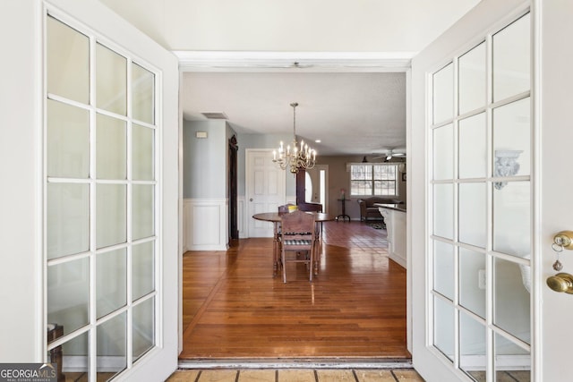 dining space featuring visible vents, a decorative wall, wainscoting, wood finished floors, and ceiling fan with notable chandelier