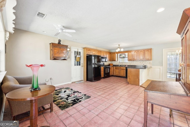 kitchen featuring dark countertops, visible vents, a sink, black appliances, and ceiling fan with notable chandelier