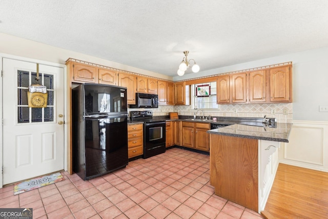 kitchen with a notable chandelier, dark countertops, backsplash, a peninsula, and black appliances