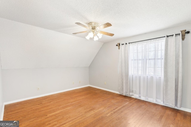 additional living space featuring a textured ceiling, a ceiling fan, vaulted ceiling, and wood finished floors