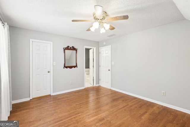 empty room with a textured ceiling, ceiling fan, wood finished floors, visible vents, and baseboards