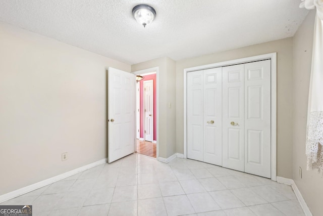 unfurnished bedroom featuring a closet, a textured ceiling, baseboards, and light tile patterned floors