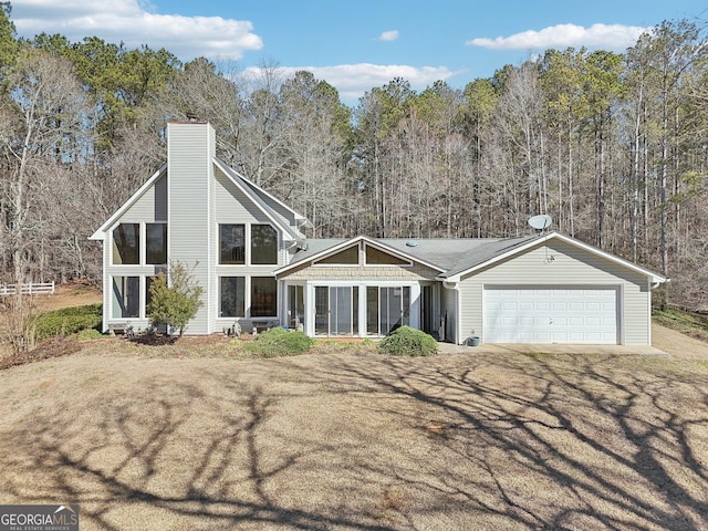 view of front of home with a chimney, a front yard, a view of trees, a garage, and driveway