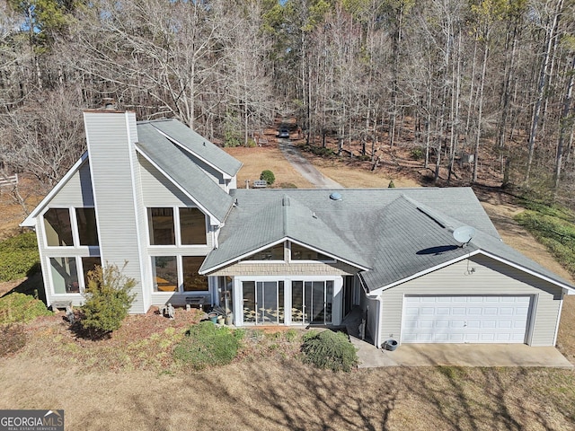 view of front of home with a sunroom, driveway, a chimney, and an attached garage