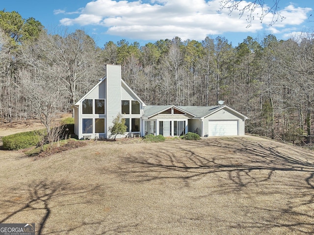 view of front facade with a wooded view, a chimney, and an attached garage