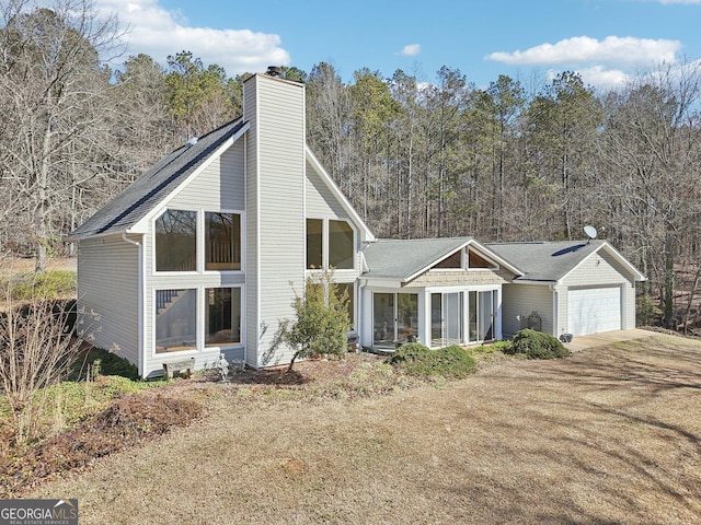 back of house featuring a chimney, an attached garage, and a lawn