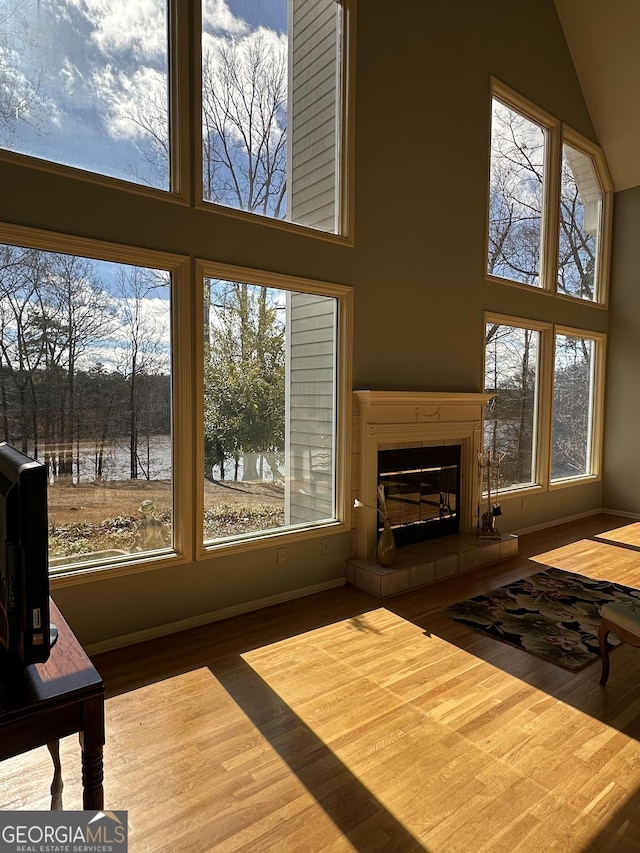 living room featuring baseboards, a high ceiling, a tiled fireplace, and wood finished floors