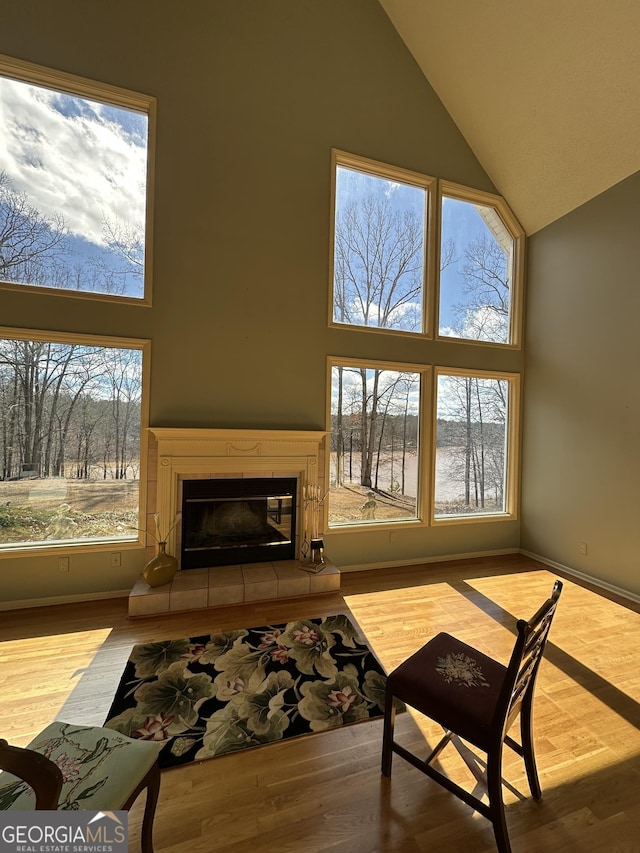 living room with high vaulted ceiling, a tile fireplace, light wood-style flooring, and a healthy amount of sunlight