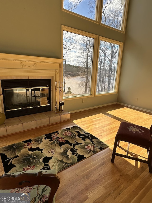 living area featuring baseboards, a tiled fireplace, wood finished floors, and a healthy amount of sunlight