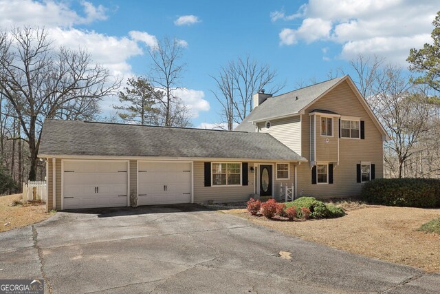 traditional home featuring an attached garage, driveway, a chimney, and a shingled roof