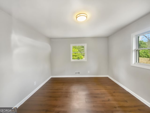 spare room featuring dark wood-style flooring, visible vents, and baseboards