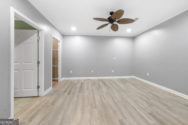 empty room featuring light wood-style floors, visible vents, baseboards, and crown molding