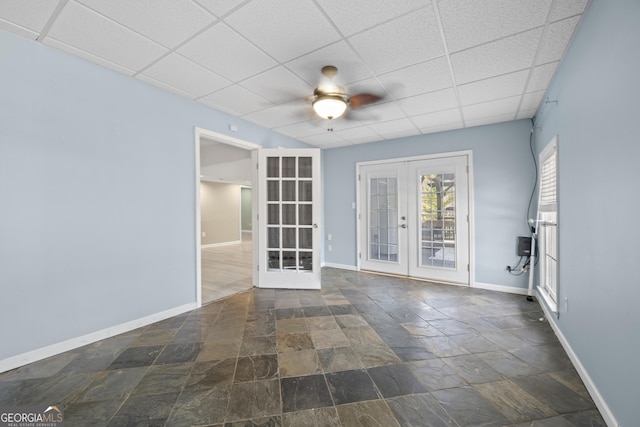 empty room featuring a drop ceiling, a ceiling fan, baseboards, french doors, and stone finish flooring