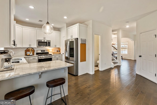 kitchen featuring stainless steel appliances, light stone countertops, decorative light fixtures, and white cabinetry