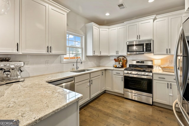 kitchen with dark wood-type flooring, a sink, white cabinets, appliances with stainless steel finishes, and light stone countertops