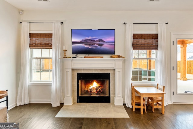 interior space with plenty of natural light, a tiled fireplace, wood finished floors, and baseboards