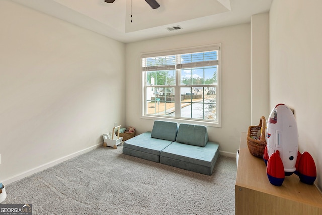 living area with baseboards, visible vents, a ceiling fan, a tray ceiling, and carpet flooring