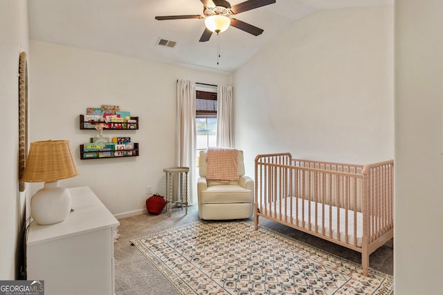 carpeted bedroom featuring lofted ceiling, visible vents, a ceiling fan, a crib, and baseboards