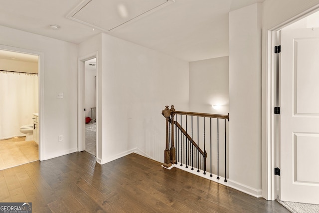 hallway featuring dark wood-style floors, attic access, baseboards, and an upstairs landing