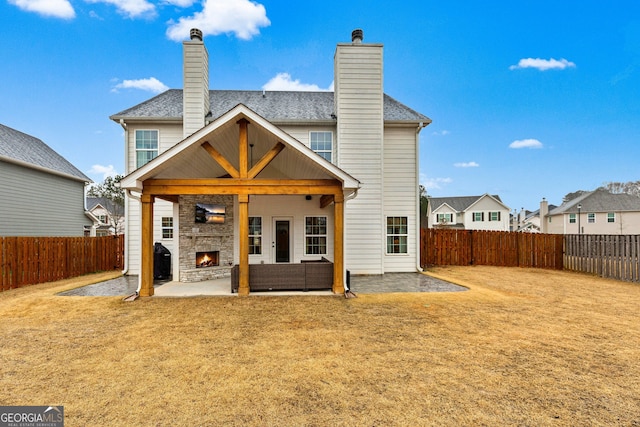 rear view of house featuring a patio, a fenced backyard, a lit fireplace, a lawn, and a residential view