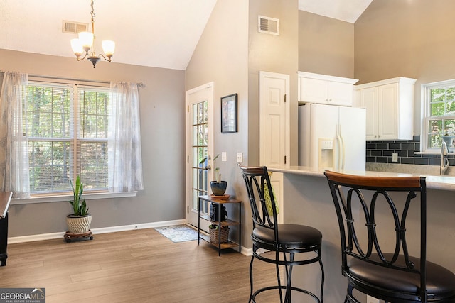 kitchen with white refrigerator with ice dispenser, white cabinets, visible vents, and light wood finished floors