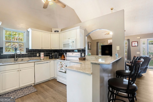 kitchen featuring white cabinetry, vaulted ceiling, a sink, white appliances, and a peninsula