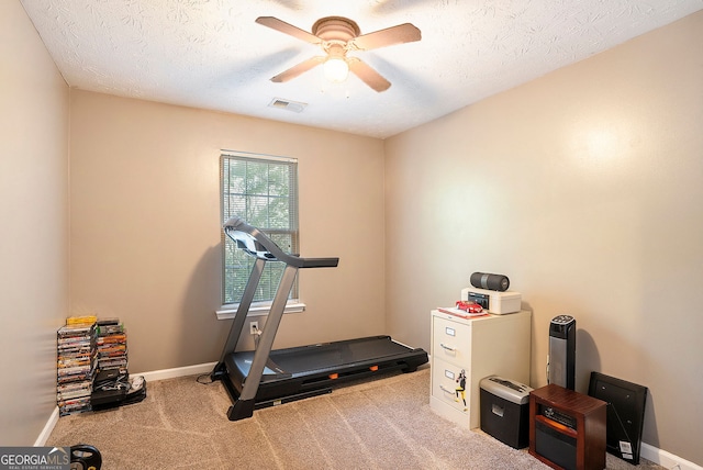 exercise room featuring baseboards, visible vents, a ceiling fan, light colored carpet, and a textured ceiling