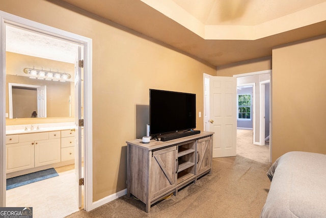 bedroom with ensuite bath, a sink, light colored carpet, and baseboards