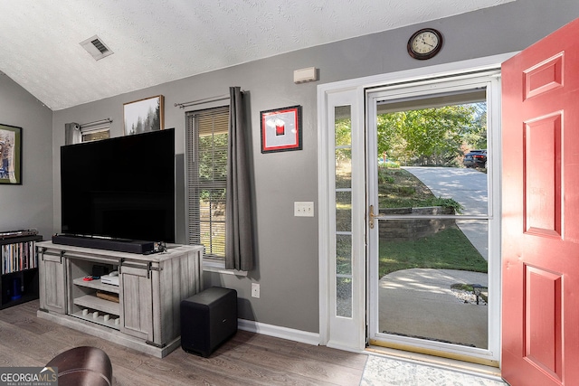 foyer entrance with baseboards, visible vents, lofted ceiling, a textured ceiling, and light wood-style floors