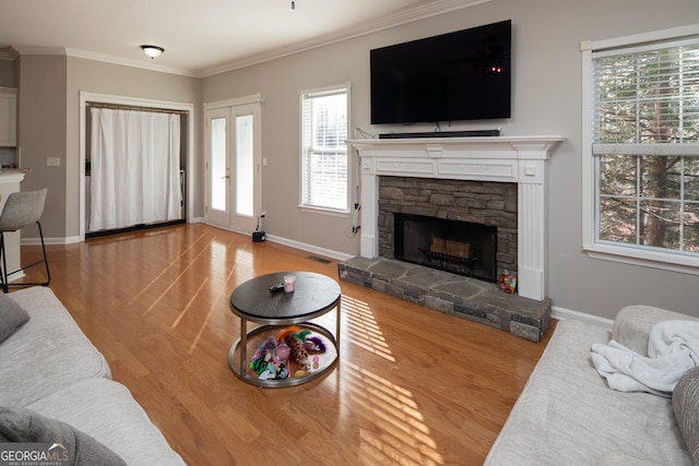 living room with crown molding, a stone fireplace, and light hardwood / wood-style floors