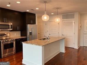 kitchen featuring light stone counters, hanging light fixtures, stainless steel appliances, and a center island with sink