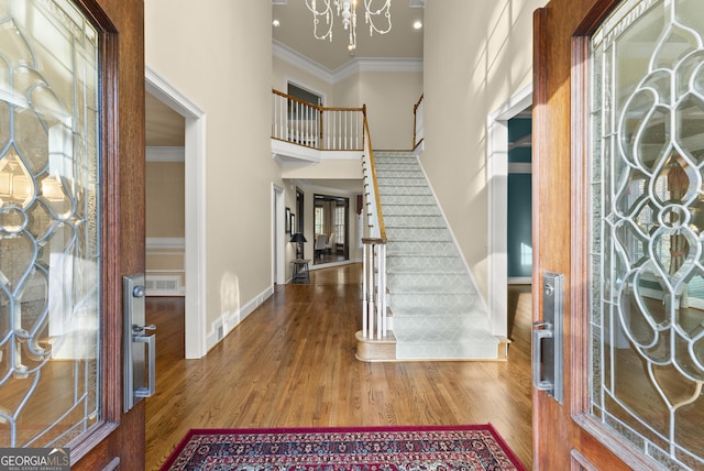 foyer with hardwood / wood-style floors, an inviting chandelier, a high ceiling, and ornamental molding