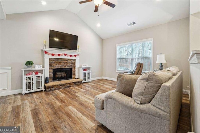 living room featuring a stone fireplace, wood-type flooring, ceiling fan, and vaulted ceiling