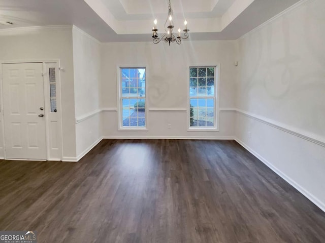 unfurnished dining area with an inviting chandelier, a tray ceiling, dark wood-type flooring, and ornamental molding