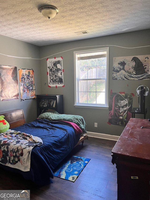 bedroom with wood-type flooring, visible vents, a textured ceiling, and baseboards