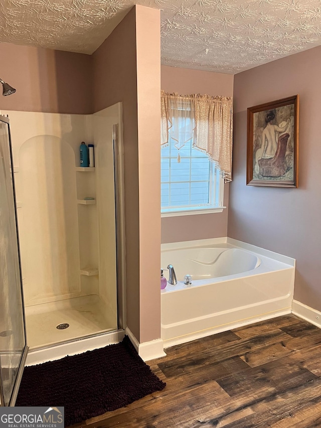 bathroom with a bath, a shower stall, a textured ceiling, and wood finished floors