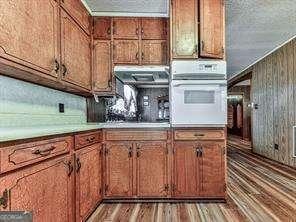 kitchen with brown cabinetry, light wood finished floors, oven, light countertops, and a textured ceiling