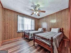 bedroom with ceiling fan, wooden walls, and wood finished floors