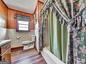 bathroom featuring wood walls, toilet, shower / tub combo, wood finished floors, and vanity