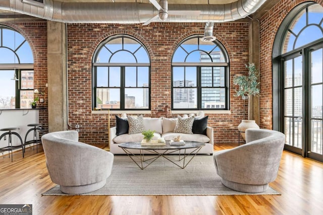 living room with a towering ceiling, brick wall, and light hardwood / wood-style flooring