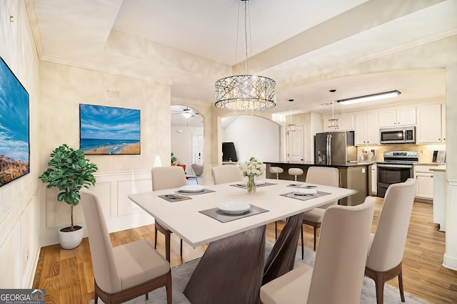 dining area featuring ornamental molding, ceiling fan, a raised ceiling, and light hardwood / wood-style flooring