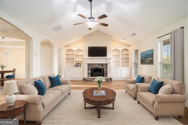 living room with lofted ceiling, ceiling fan, built in features, and a stone fireplace