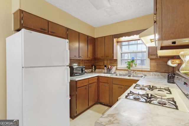 kitchen with sink, decorative backsplash, white refrigerator, gas cooktop, and a textured ceiling