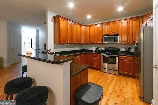 kitchen with a breakfast bar area, ornamental molding, appliances with stainless steel finishes, kitchen peninsula, and light hardwood / wood-style floors