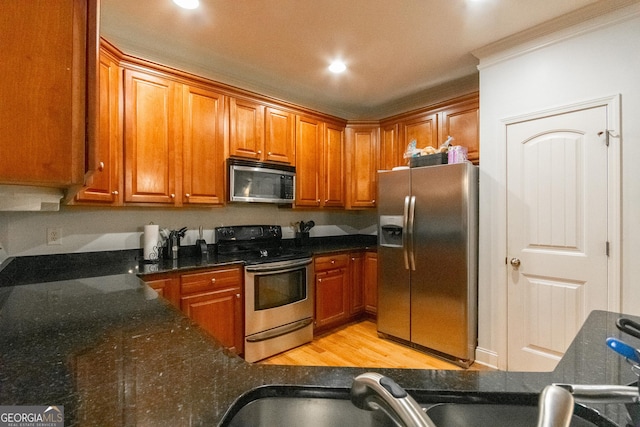 kitchen featuring stainless steel appliances, crown molding, dark stone countertops, and light hardwood / wood-style flooring