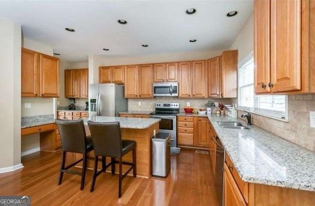 kitchen featuring sink, a breakfast bar area, stainless steel appliances, a center island, and light stone countertops