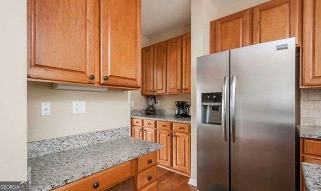 kitchen featuring light stone counters, tasteful backsplash, and stainless steel refrigerator with ice dispenser