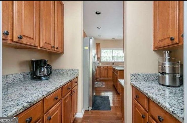 kitchen featuring sink, stainless steel refrigerator, hardwood / wood-style floors, and light stone counters